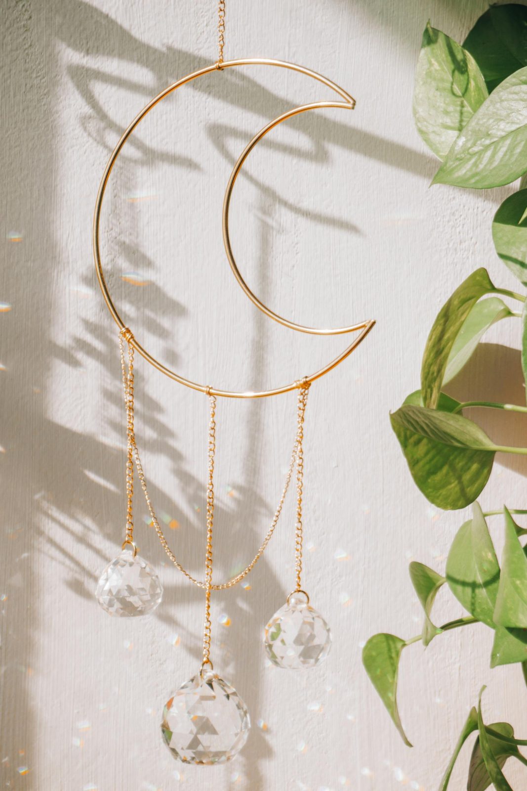 A close-up of a crescent moon suncatcher with crystals hanging, accentuated by sunlight and foliage.